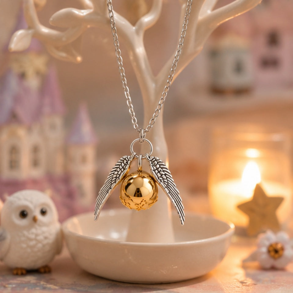 Collier vif d’or inspiré d’un univers magique avec pendentif doré brillant et ailes argentées délicates ✨ Bijou fantaisie féerique suspendu sur un présentoir dans une ambiance chaleureuse et enchantée avec bougie, chouette blanche et décor pastel. Parfait pour les fans de magie et d’univers fantastiques.