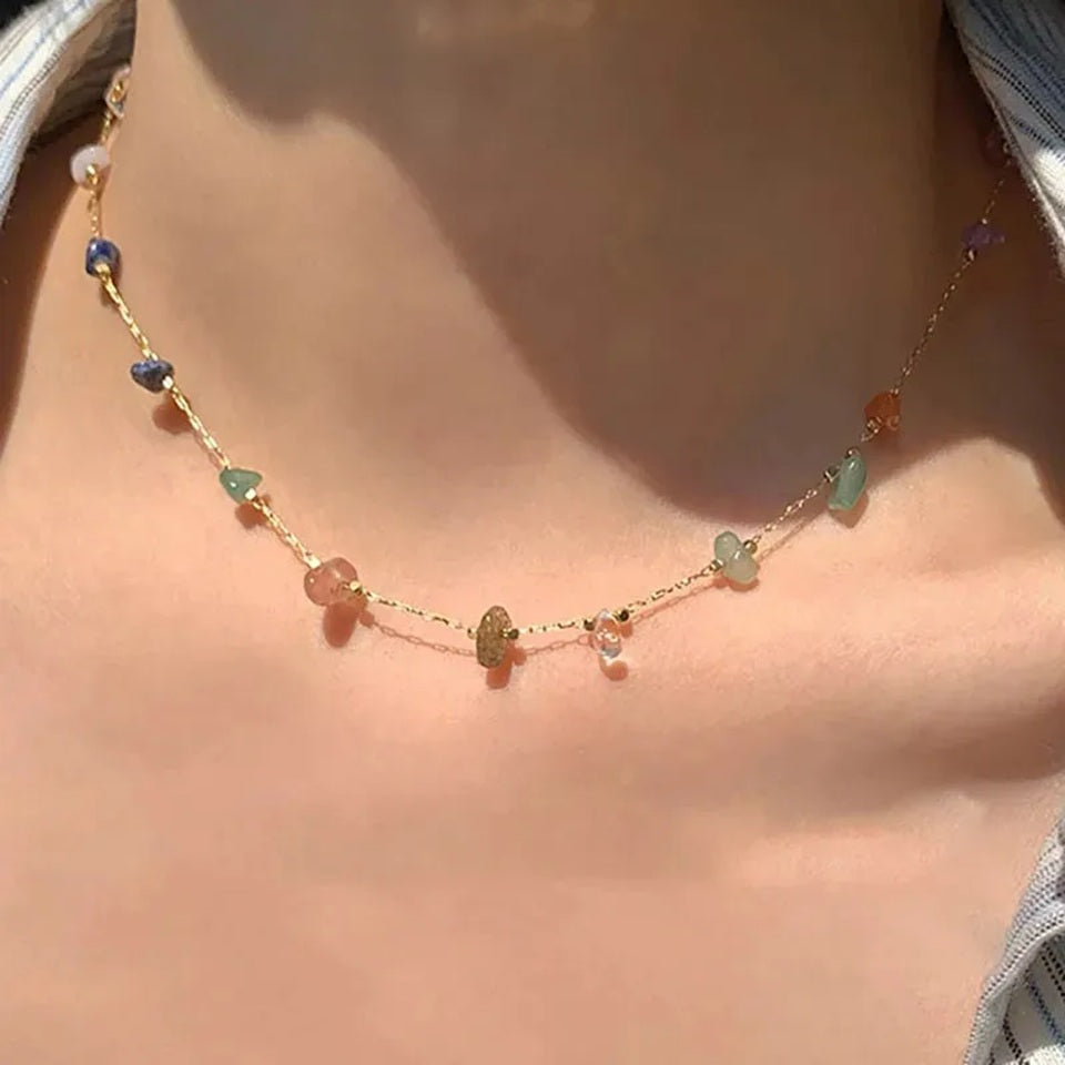 Gros plan d'un collier doré fin orné de petites pierres colorées, porté par une femme. Ambiance douce et chaleureuse. Style mignon, moderne et plein de poésie