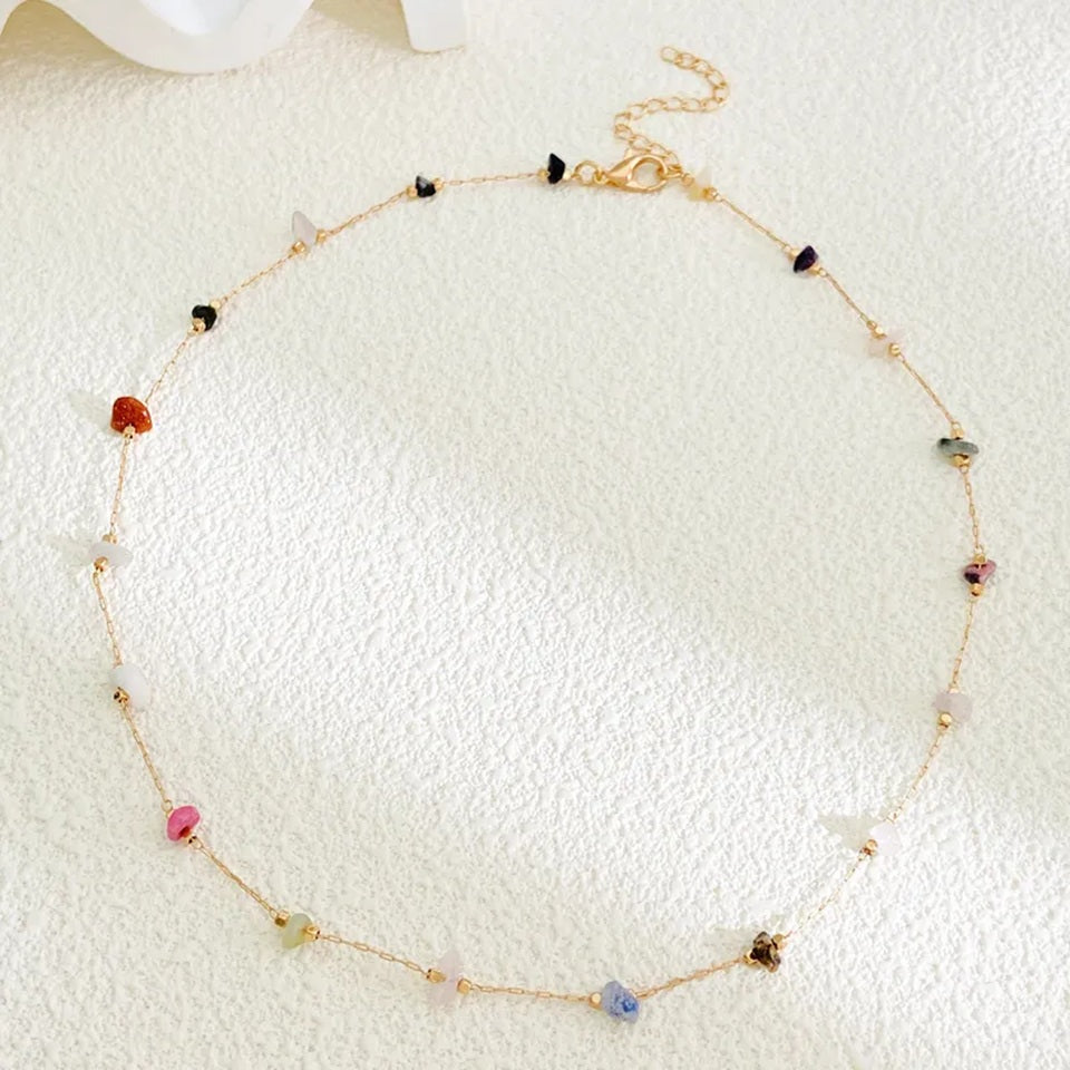 un collier doré orné de pierres naturelles colorées, présenté sur un tissu beige
