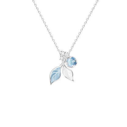 un collier argenté dont le pendentif représente de délicates feuilles bleues et d'une perle aux reflets bleutées. L'ensemble est poétique.