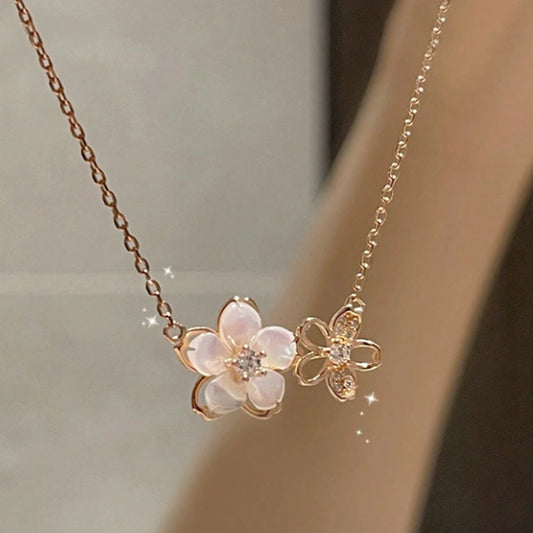 un collier rose gold très clair avec un pendentif double fleurs de sakura. Une avec des pétales blancs brillants et l'autre en métal avec des strass scintillants.