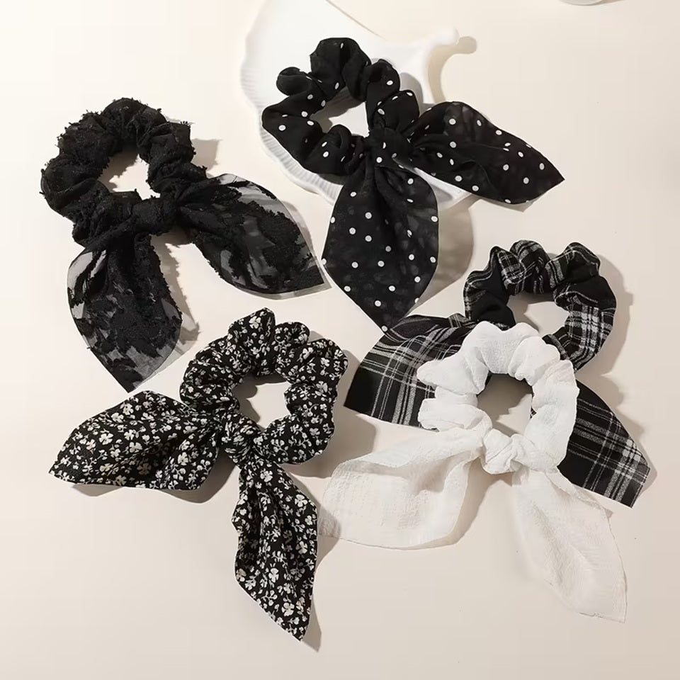 Présentation de plusieurs chouchous blancs et noirs avec différents motifs variés : lignes, fleurs, pois, brodés ou gaufrés. Ils sont adorables et ajoutent une touche d'élégance à n'importe quelle coiffure.