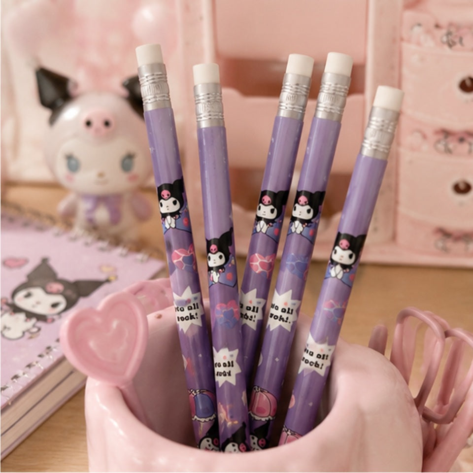 Quatre crayons à papier violets décorés de Kuromi sont rangés dans un pot à crayons rose en forme de tasse. L'ensemble est posé sur un bureau kawaii avec un carnet illustré, une petite figurine, des accessoires roses et un fond pastel créant une ambiance douce et chaleureuse