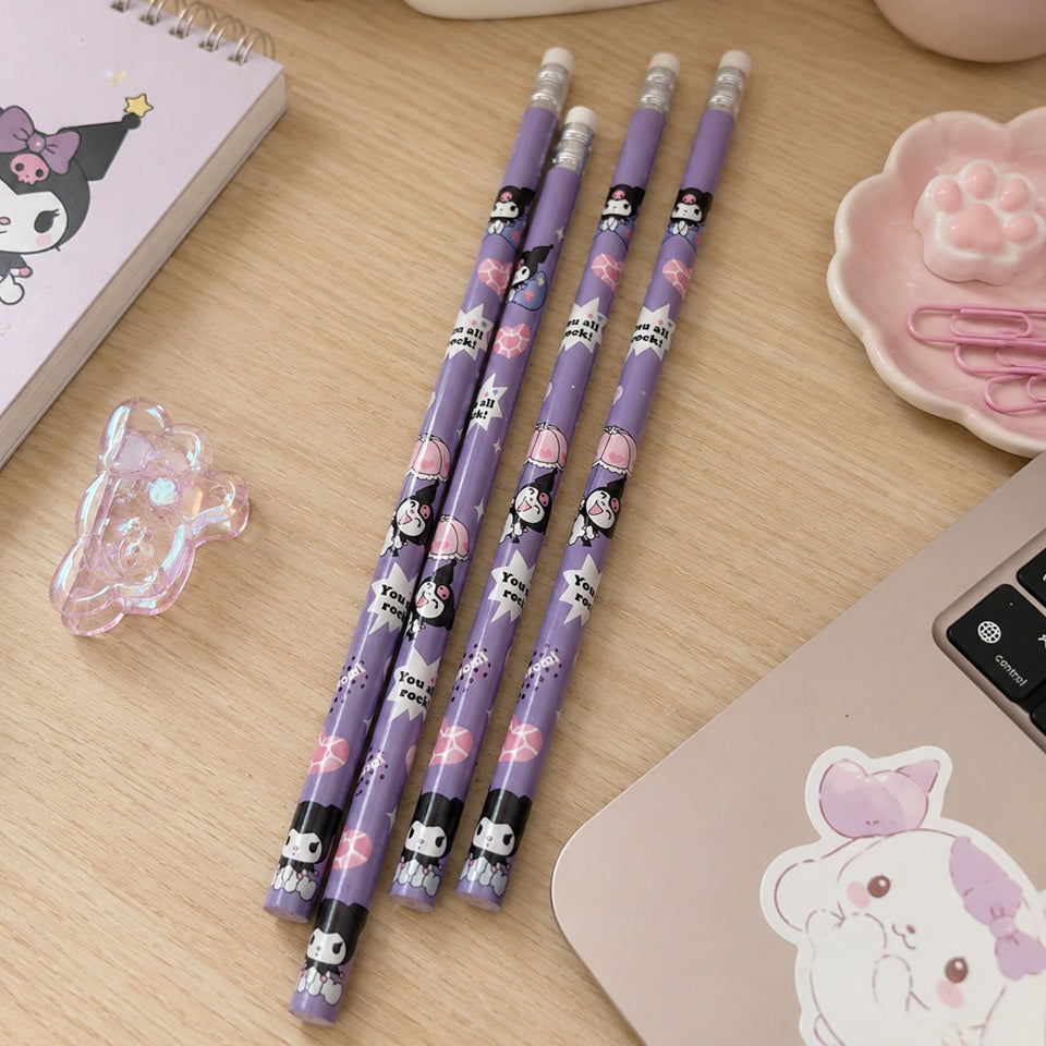 Quatre crayons à papier kawaii violets ornés de personnages Kuromi sont disposés sur un joli bureau en bois clair. Autour d'eux se trouvent un pot à crayons en céramique avec un cœur rose, un carnet assorti, une petite figurine, une plante fleurie, un repose-trombones en forme de patte, un ordinateur portable décoré d'un sticker pastel et plusieurs accessoires de papeterie roses. L'ensemble crée une ambiance douce, mignonne et chaleureuse, idéale pour un espace de travail ou d'étude.