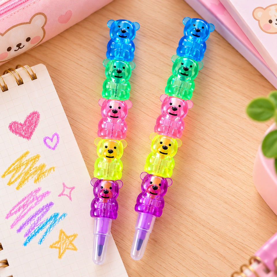 Deux crayons de couleur kawaii en forme d'oursons empilables, composés de cinq petits ours translucides aux couleurs bleu, vert, rose orangé, jaune et violet. Présentés sur un bureau en bois clair avec un carnet de dessins et une trousse rose, ces crayons originaux et amusants offrent un gain de place grâce à leur système d'empilage. Papeterie kawaii adorable, idéale pour le coloriage, le dessin et les amoureux des accessoires mignons.