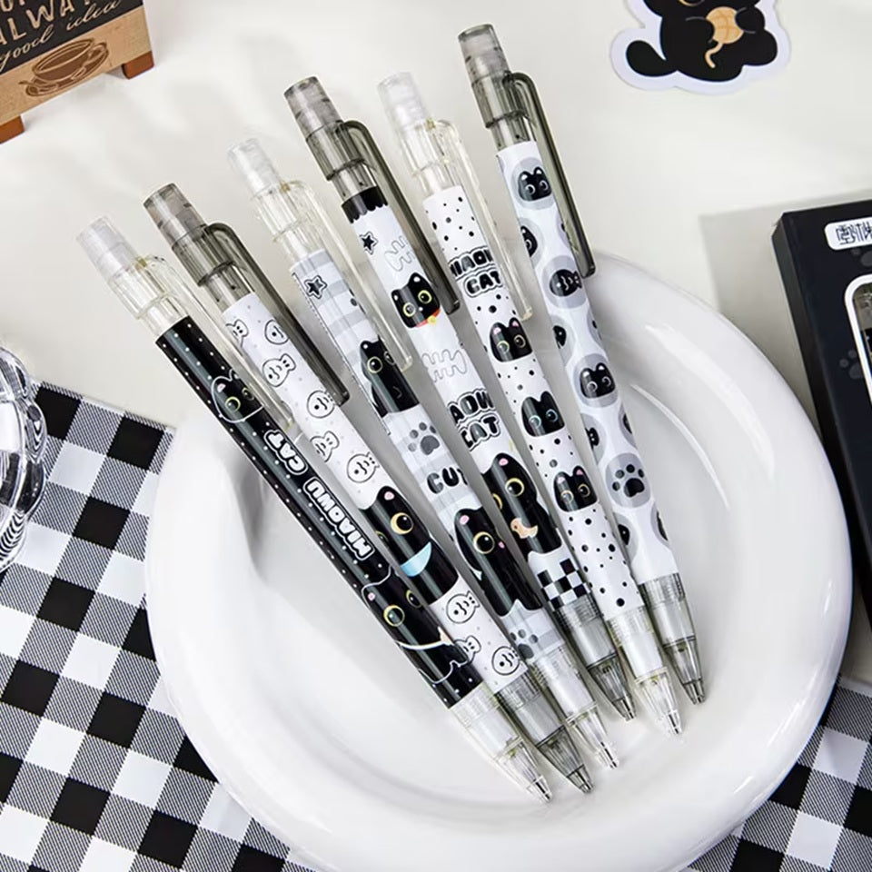 des critériums noirs et blancs au design de chats façon chibi. Ils sont posés dans une assiettes sur une table décorée d'éléments mignons.