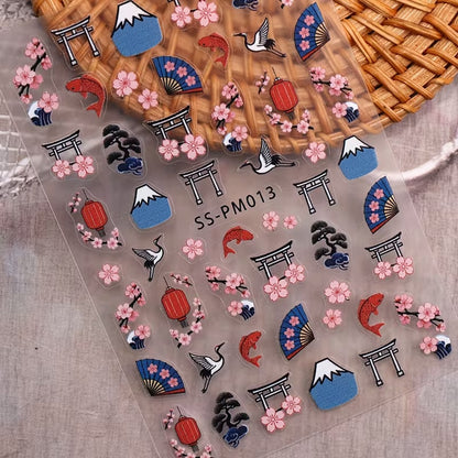 une planche de sticker pour nail art sur le thème du japon : sakura, tori, éventails, carpe koi et mont fuji posés sur une table grise asur un support en rotin. Colorés et mignons, ils apportent une touche exotique et original sur vos ongles.