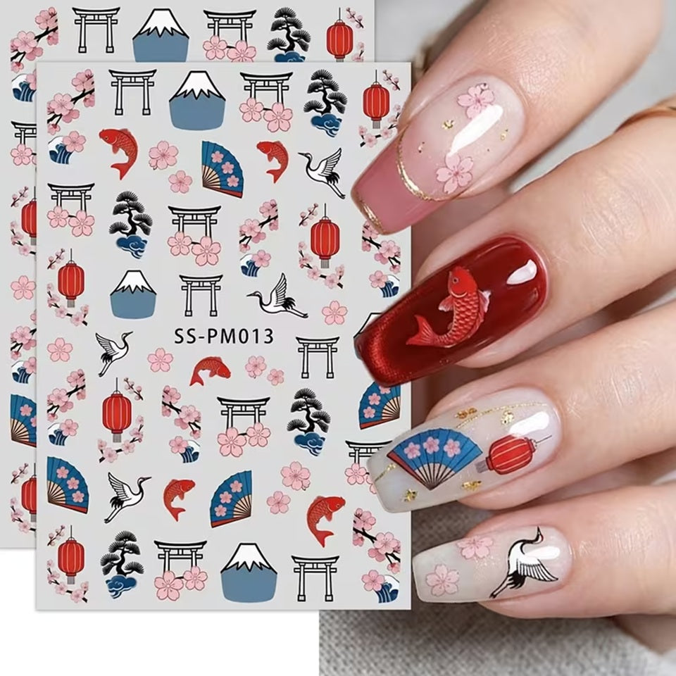 une planche de sticker pour nail art sur le thème du japon : sakura, tori, éventails, carpe koi et mont fuji présentés posés sur des ongles vernis rouge et blancs. Ils sont colorés et rappellent Le japon et son folklore.