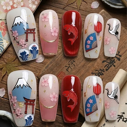 Des ongles vernis en rouge et blancs sur lesquels sont posés des stickers de nail art sur le thème du Japon : fleurs de sakura, carpe koi, éventail, tori et mont fuji.