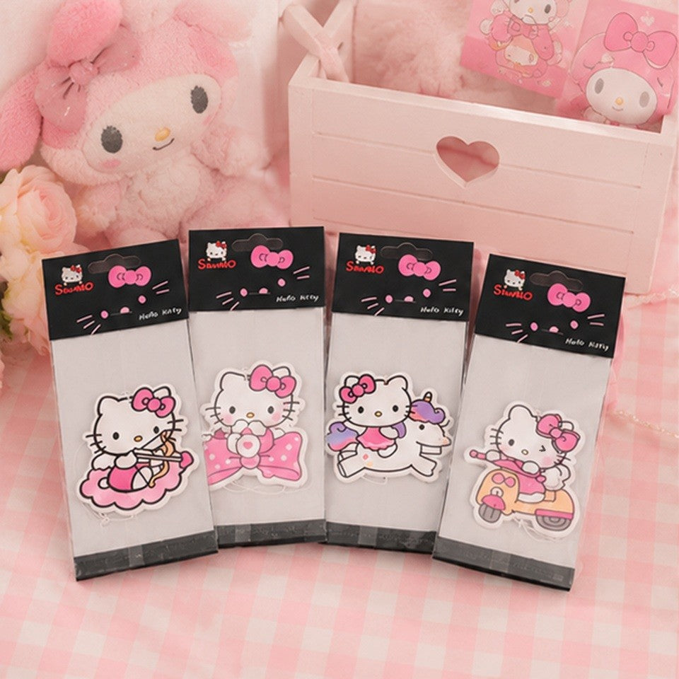 un lot de désodorisants à suspendre en forme de l'adorable Hello Kitty posés sur une jolie table avec une nappe roche vichy., dans un décor rose, pastel et mignon.