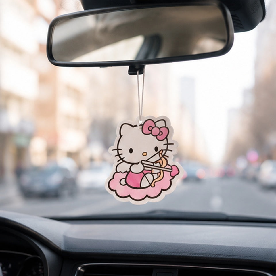 un désodorisant en forme de hello kitty habillé en cupidon, avec un arc et une flèche coeur suspendu à un rétroviseur intérieur d'une voiture, qui roule sur une route de ville.