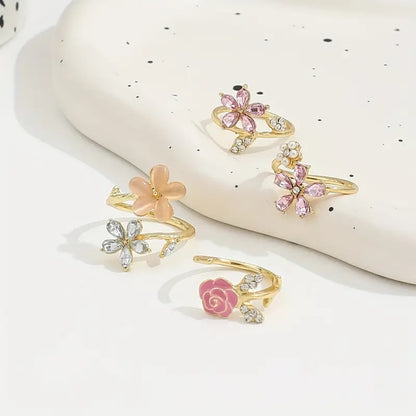 un ensemble de 4 bagues en alliage doré au design de fleurs roses élégantes et de strass brillants roses et argentés avec des perles. L'ensemble est romantique et féminin