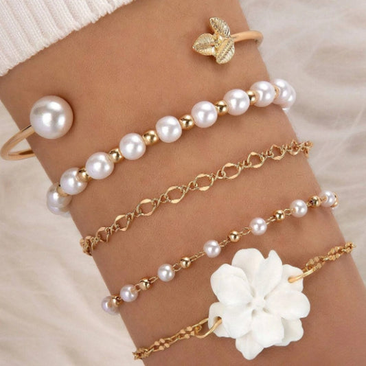 un ensemble de bracelets dorés avec des perles blanches et une fleur blanche. Style bohème, chic et élégant. 
