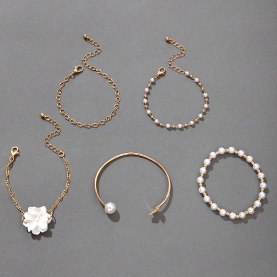un ensemble de bracelets dorés avec des perles blanches et une fleur blanche. Style bohème, chic et élégant. 