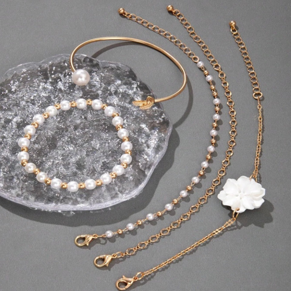 un ensemble de bracelets dorés avec des perles blanches et une fleur blanche. Style bohème, chic et élégant. 