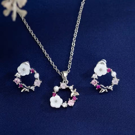 un ensemble argenté de boucles d'oreilles et d'un collier composés d'une fleur blanche, de strass roses et d'un papillon qui forment, ensemble, une jolie ronde enchantée.
