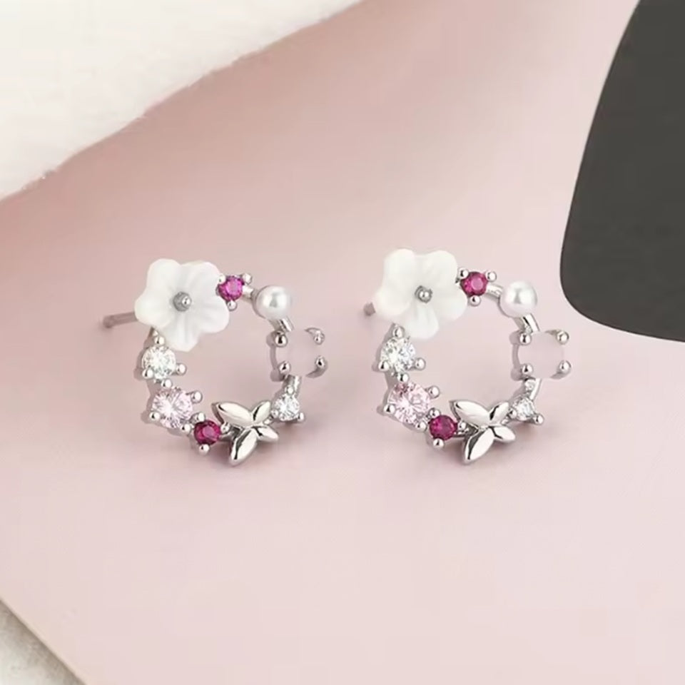 un ensemble argenté de boucles d'oreilles et d'un collier composés d'une fleur blanche, de strass roses et d'un papillon qui forment, ensemble, une jolie ronde enchantée.