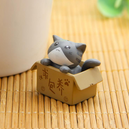 des figurines de chat bien lovés dans leur boite en carton : gris, noir, blanc ou roux, ils sont adorables. Parfait pour décorer une pièce avec style et mignonnerie