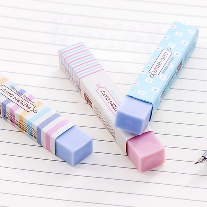 Gros plan sur trois jolies gommes rectangulaires rose et bleu au motif de lignes colorées et de fleurs blanches posées à cheval sur une feuille.
