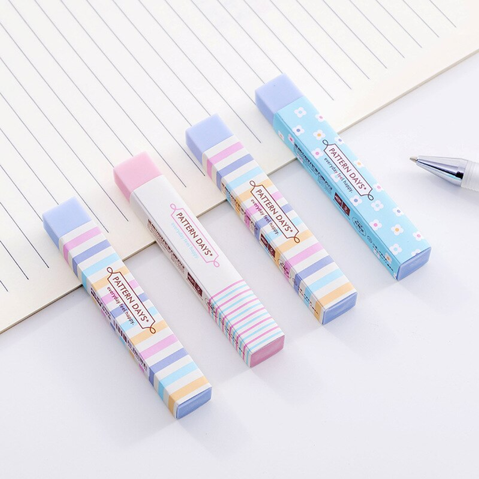 Quatre jolies gommes rectangulaires rose et bleu au motif de lignes colorées et de fleurs blanches présentées sur une feuille posées sur un bureau blanc.