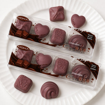 Lot de 4 gommes en forme de chocolats réalistes, présentées dans une boîte transparente sur une assiette blanche, papeterie kawaii originale effet trompe-l’œil.