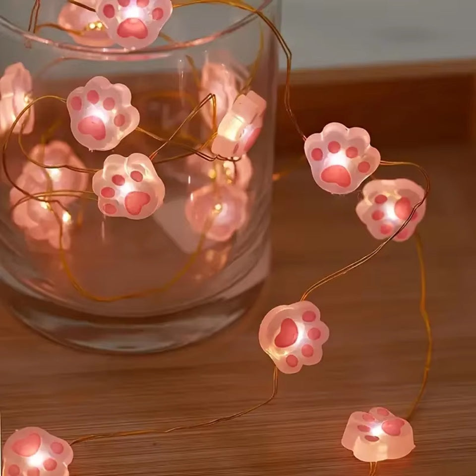 une guirlande LED en forme de pattes de chat roses toutes mignonnes. Elle diffuse une lumière jaune douce et chaleureuse. Idéal pour un coin cocooning.