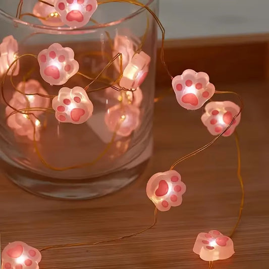 une guirlande LED en forme de pattes de chat roses toutes mignonnes. Elle diffuse une lumière jaune douce et chaleureuse. Idéal pour un coin cocooning.
