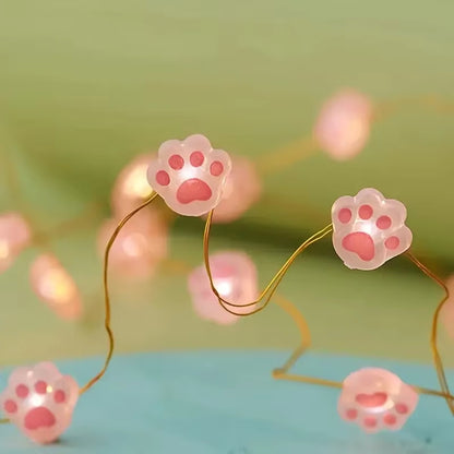 une guirlande LED en forme de pattes de chat roses toutes mignonnes. Elle diffuse une lumière jaune douce et chaleureuse. Idéal pour un coin cocooning.