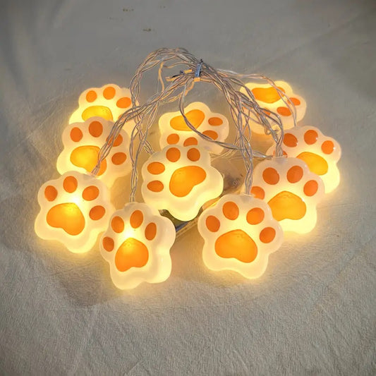 une guirlande LED en forme de pattes de chat roses toutes mignonnes. Elle diffuse une lumière jaune douce et chaleureuse. Idéal pour un coin cocooning.