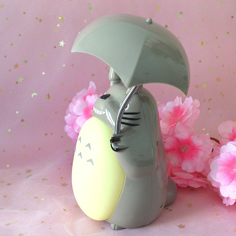une merveilleuse lampe en forme de Totoro qui tient son parapluie.Il a son célèbre sourire et la lumière peut être allumée sous son parapluie ou sur son ventre