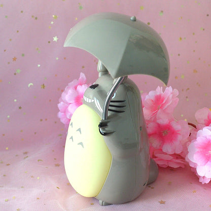 une merveilleuse lampe en forme de Totoro qui tient son parapluie.Il a son célèbre sourire et la lumière peut être allumée sous son parapluie ou sur son ventre