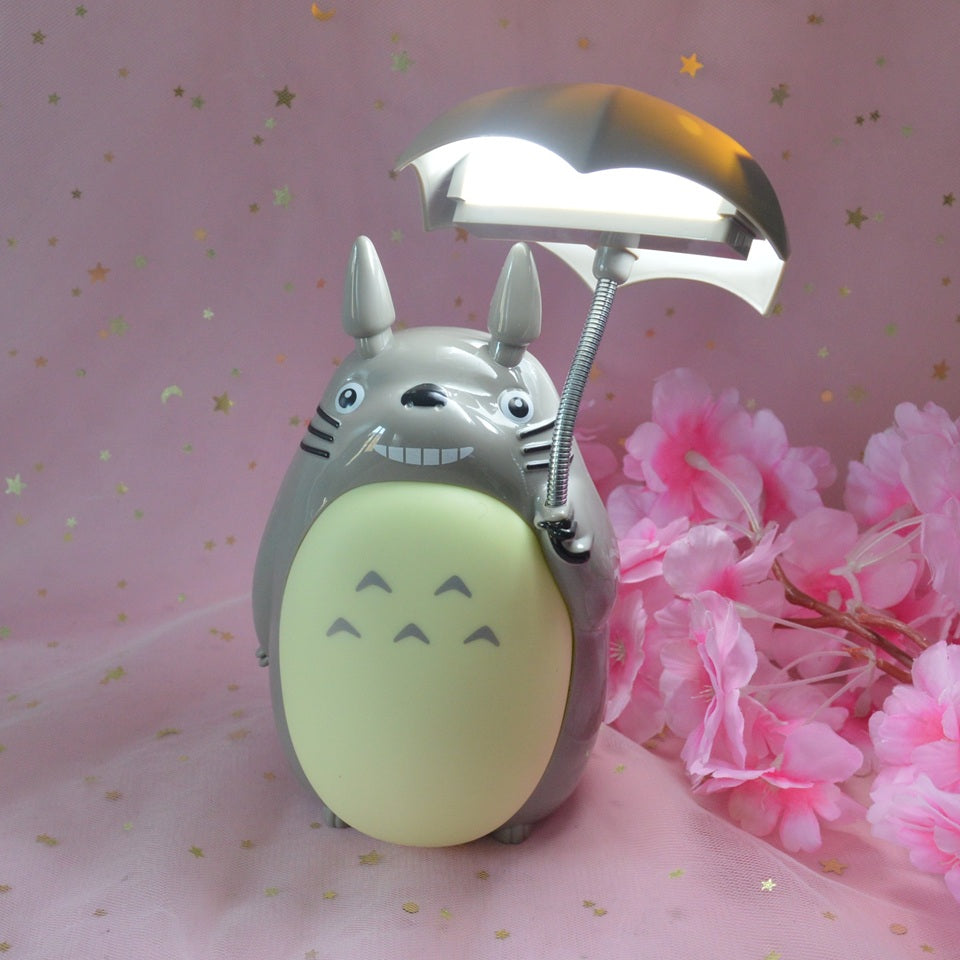une merveilleuse lampe en forme de Totoro qui tient son parapluie.Il a son célèbre sourire et la lumière peut être allumée sous son parapluie ou sur son ventre