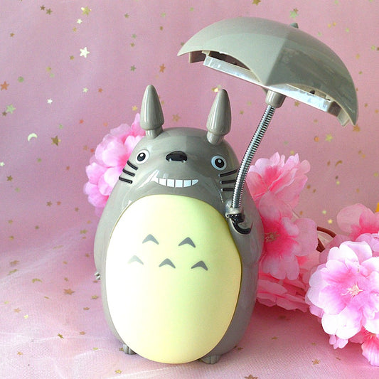 une merveilleuse lampe en forme de Totoro qui tient son parapluie.Il a son célèbre sourire et la lumière peut être allumée sous son parapluie ou sur son ventre