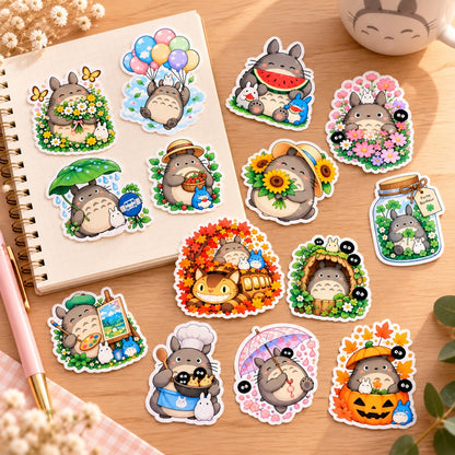Stickers Totoro kawaii colorés avec fleurs, tournesols, pluie et scènes d’automne, disposés sur un carnet et un bureau en bois clair dans un décor doux et naturel.