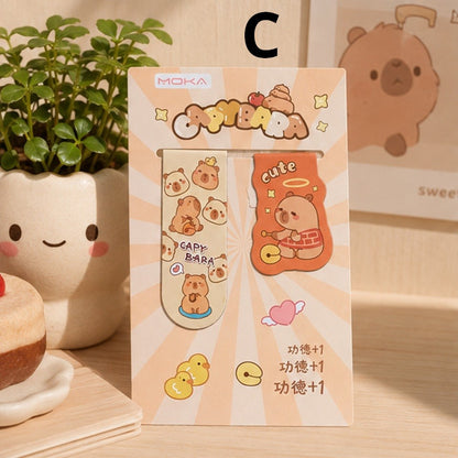 Lot de 2 marque-pages magnétiques capybara kawaii aux tons beige et orange, présenté dans un décor cosy avec plante verte et accessoires pastel.