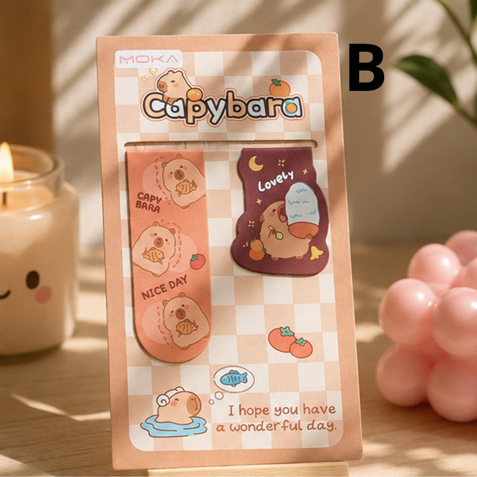 Duo de marque-pages magnétiques capybara kawaii rose et marron, présenté sur un bureau en bois dans une ambiance douce et chaleureuse.