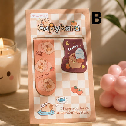 Duo de marque-pages magnétiques capybara kawaii rose et marron, présenté sur un bureau en bois dans une ambiance douce et chaleureuse.