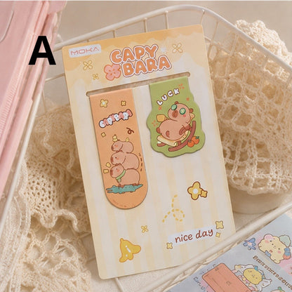 Lot de 2 marque-pages capybara kawaii aux couleurs pastel orange et vert, présenté dans une corbeille avec tissu en maille pour une ambiance cocooning.