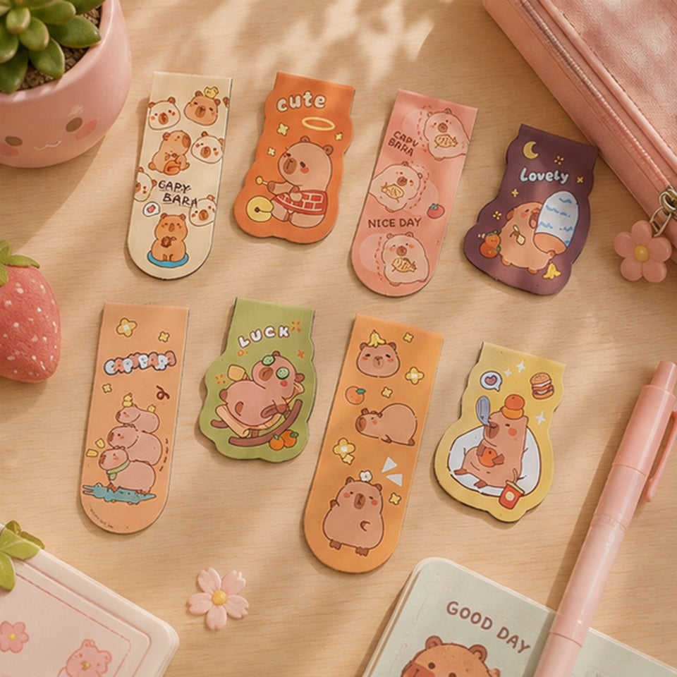 Lot complet de 8 marque-pages magnétiques capybara kawaii posé sur un bureau en bois clair, entouré de papeterie et petites décorations pastel.