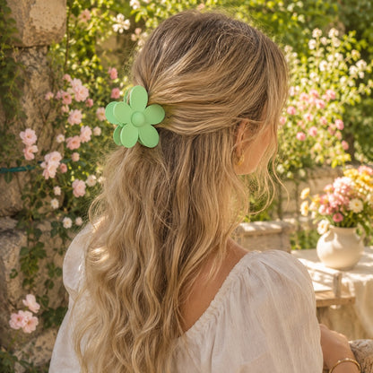 Femme portant une pince à cheveux fleur verte en demi-queue dans un jardin fleuri en été. Grande barrette florale vert pastel de taille moyenne, idéale pour une coiffure bohème, romantique et élégante.