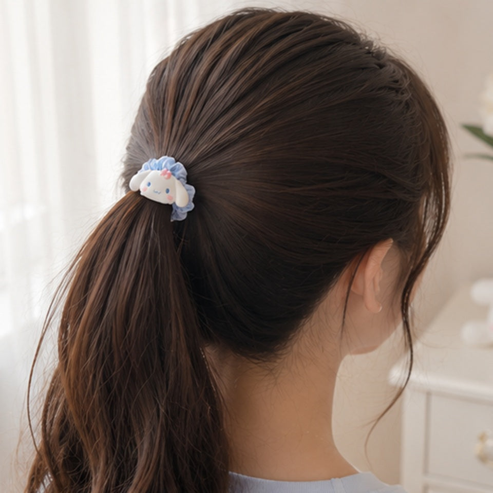 Un joli élastique à cheveux kawaii inspirés de l'univers Sanrio, avec le personnage Cinnamoroll. Le chouchou est confectionné dans un tissu satiné aux couleurs pastel bleu. Il est attaché sur une queue de cheval dans les cheveux d'une jeune femme.