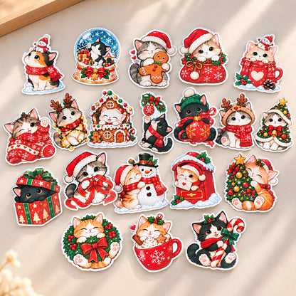Collection de 20 stickers chats de Noël kawaii aux illustrations variées : chatons avec bonnets de Père Noël, cadeaux, sapins, bonhomme de neige, pain d’épices et chocolat chaud. Autocollants aux contours blancs, disposés sur un fond beige clair.