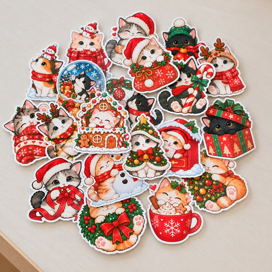 Lot de stickers chats de Noël kawaii aux illustrations variées : chatons avec bonnets de Père Noël, cadeaux, sapins, couronnes, bonhomme de neige et tasse de chocolat chaud, avec contours blancs, disposés sur un fond clair.