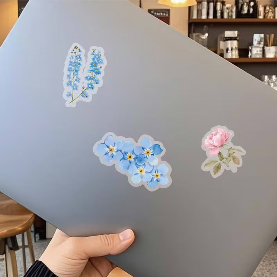 un lot de stickers représentant diverses fleurs de couleurs et formes variées collés sur un oridnateur portable. En rose et en bleu, ils ajoutent une douce touche florale.
