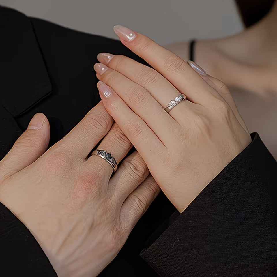 un lot de 2 bagues argentées complémentaires, l'une représente des ailes d'ange avec un strass blanc, l'autre des ailes de démon avec un strass noir.