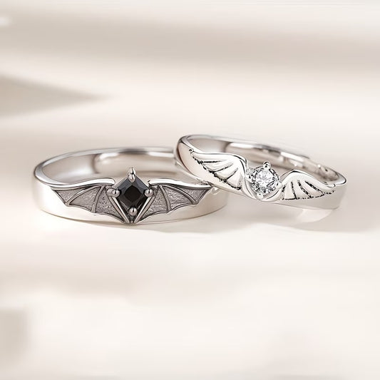 un lot de 2 bagues argentées complémentaires, l'une représente des ailes d'ange avec un strass blanc, l'autre des ailes de démon avec un strass noir.