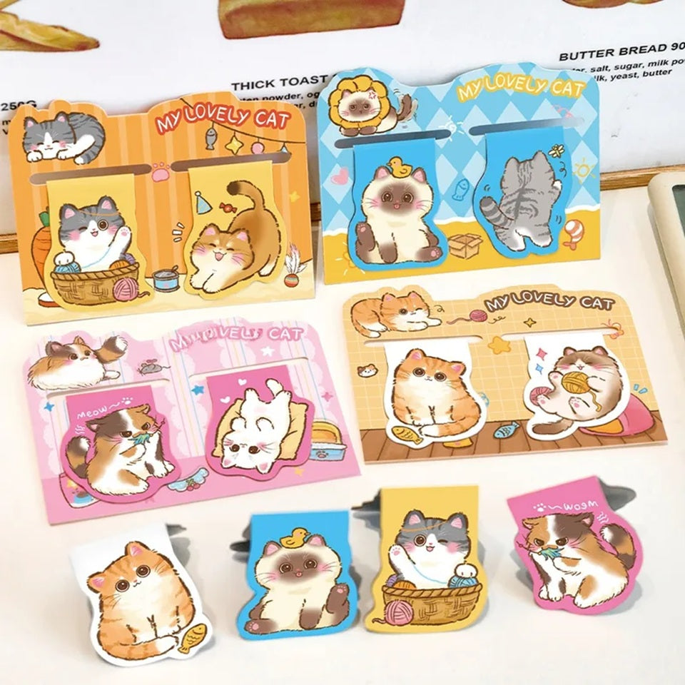Des marque-pages aimantés en forme de chats  gris, brun, calico, roux, hyper mignons dans des poses et scénettes amusantes et adorables posés sur une table blanche. Ils égayent la papeterie avec leur expression trop mignonnes.