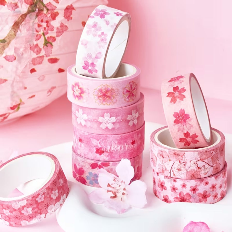 Gros plan sur des washi tape au motif de fleurs de sakura rose posés sur une table rose.  Idéal pour une touche florale et romantique qui rappelle les cerisiers en fleurs du Japon.