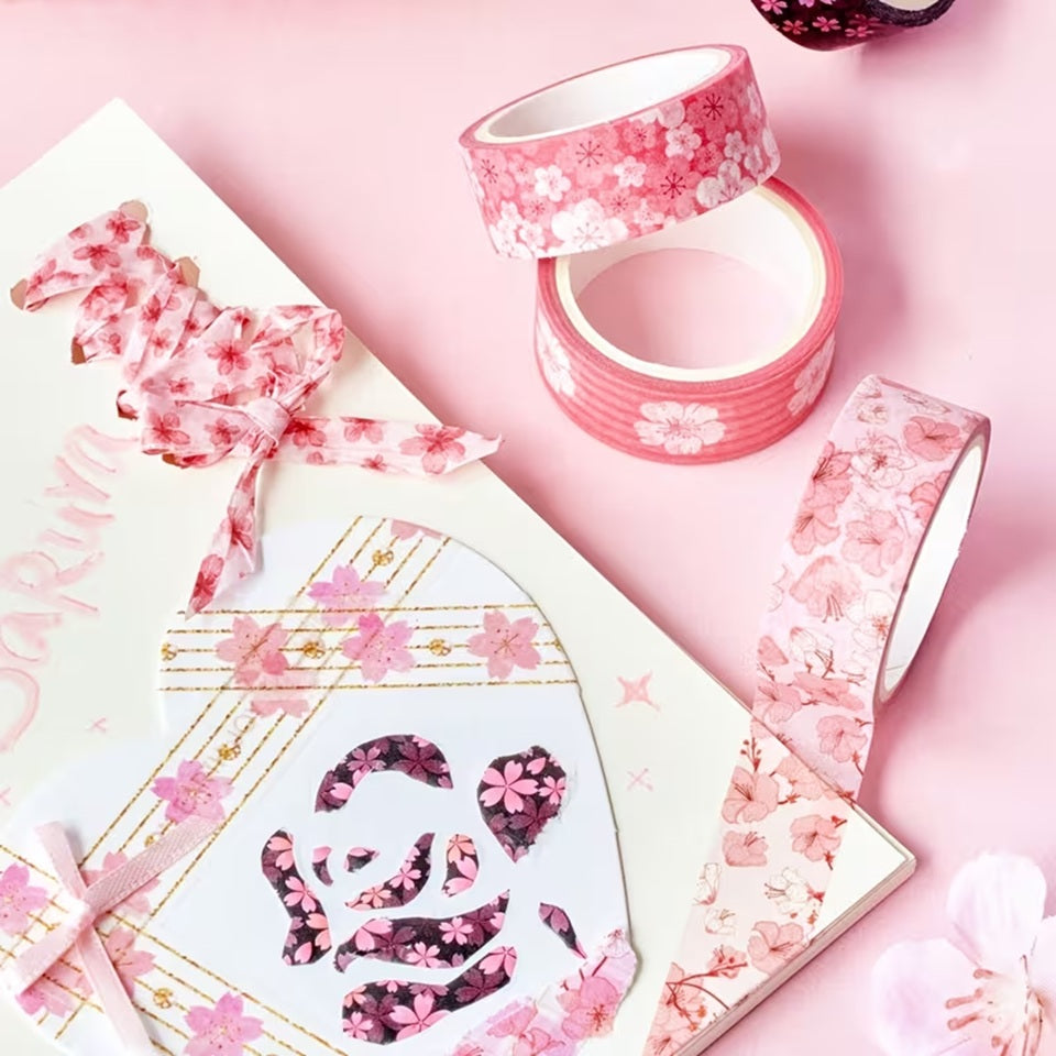 des washi tape au motif de fleurs de sakura rose posés sur une table rose. Sur un cahier, des morceaux de wwashi tape sont collés.