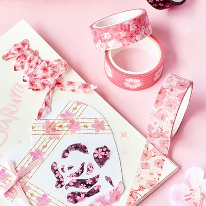 des washi tape au motif de fleurs de sakura rose posés sur une table rose. Sur un cahier, des morceaux de wwashi tape sont collés.